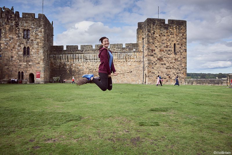 ©VisitBritain - Young woman hovering on a broomstick in the Outer Bailey of Alnwick Castle, Northumberland