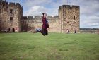 ©VisitBritain - Young woman hovering on a broomstick in the Outer Bailey of Alnwick Castle, Northumberland